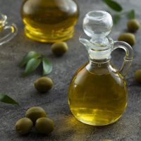 ظرف روغن زیتون در کنار برگ و میوه زیتون - خواص روغن زیتون