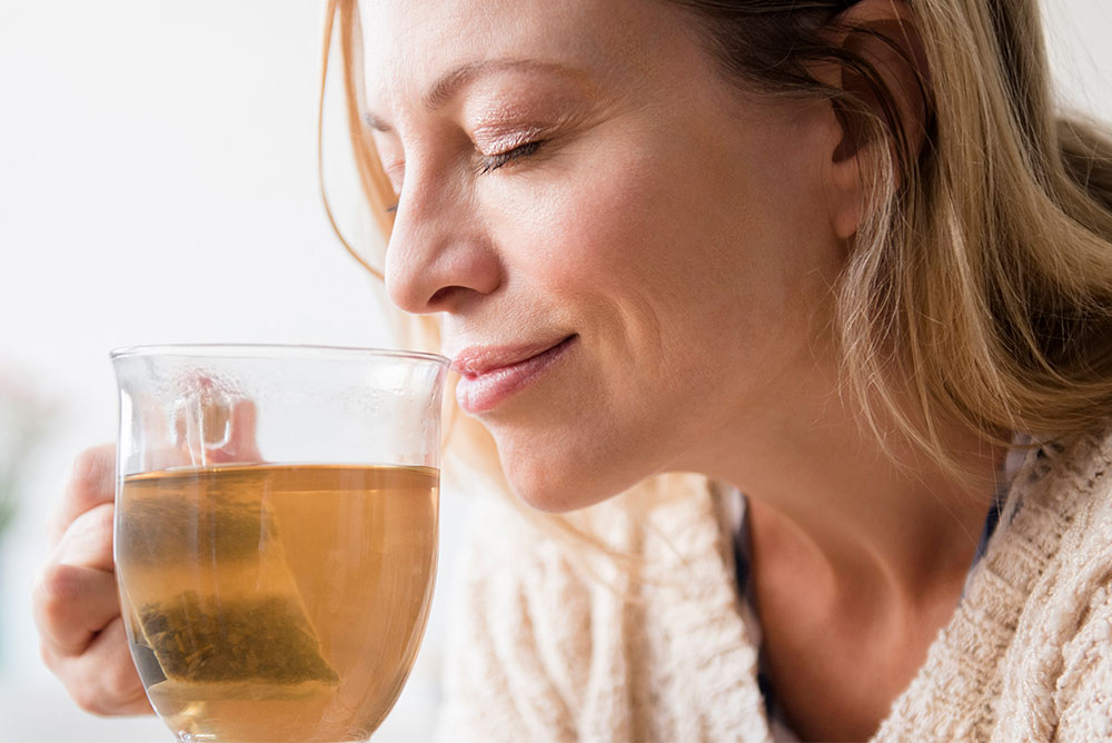 زنی در حال بوییدن دمنوش گیاهی خود -کاهش استرس و فشار عصبی